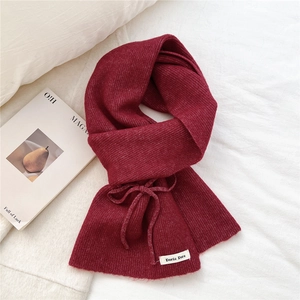 Detail of burgundy knit scarf showing bow decoration and soft ribbed texture on white bedding