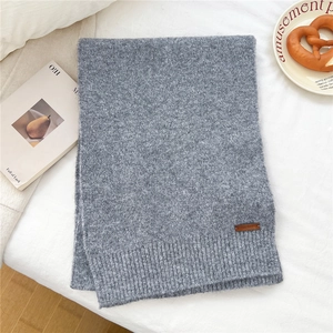 Close-up of soft grey knit scarf detail featuring a brown leather brand tag on ribbed edge