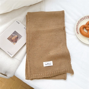 Detail eines kamelfarbenen Strickschals mit bunten Tupfern und dekorativem weißen Markenlabel