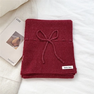Detail of red ribbed knit scarf with bow decoration and brand label on white fabric