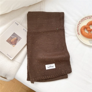 Detaillierte Textur des dunkelbraunen Strickschals mit Noppengarn und weißem Logo-Label