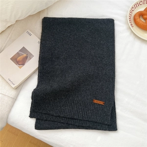 Detailed texture of dark grey knit scarf with premium leather brand label and ribbed hem