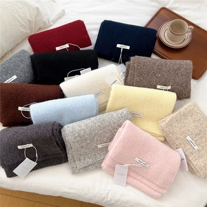 Close-up of soft wool knit scarves in multiple colors with brand labels on a white bed