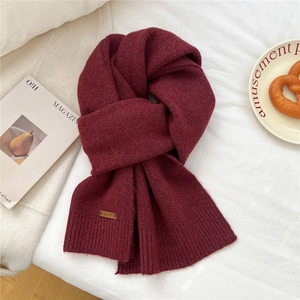Macro shot of burgundy knitted scarf with leather logo patch and ribbed edge detail