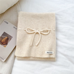 Detail of beige knitted scarf with bow decoration and brand label on white fabric