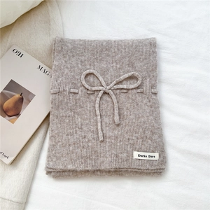 Detail of oatmeal knit scarf showing ribbed texture and a soft decorative bow accent
