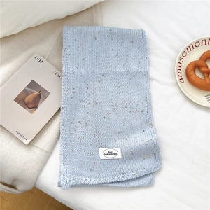 Detailansicht eines hellblauen Grobstrickschals mit bunten Tupfen und Markenetikett