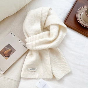Detail view of cream wool knit scarf texture with a brand label on soft white fabric