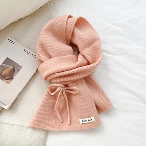Close-up of pink ribbed knit scarf detail with bow accent and branded fabric label