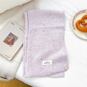 Detail eines lila Strickschals mit bunten Sprenkeln und einem weißen Markenetikett auf Stoff