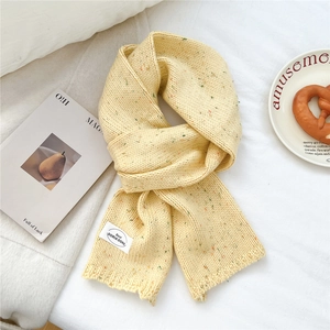 Nahaufnahme des cremefarbenen Strickschals mit bunten Tupfen und weißem Stoffetikett