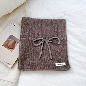 Close-up of brown ribbed knit scarf with bow decoration and brand label detail