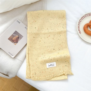 Detail eines gelben Strickschals mit bunten Polka-Dot-Jacquard und weißem Label