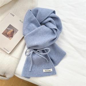 Close-up of soft light blue ribbed knit scarf with woven brand label on white fabric
