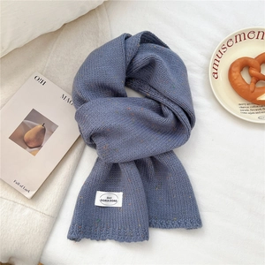 Nahaufnahme von blauem Strickschal mit bunten Punkten und weißem Etikett auf Stoff