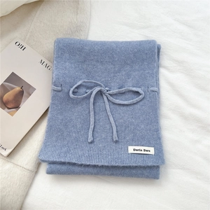 Detail of light blue knitted scarf texture with soft bow decoration and brand tag