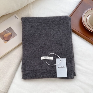 Close-up of soft dark grey wool knit scarf texture with brand tag in cozy home setting