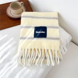 Detail of soft striped wool scarf with fringe and a woven brand label on white bedding