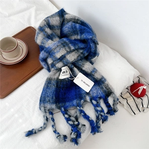 Detail shot of soft blue and grey checkered knit scarf with long tassels on a white bed