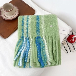 Close-up of green and blue striped wool scarf with long tassels on white bed