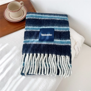 Close-up of blue and white striped wool scarf with fringe and brand label on white bed