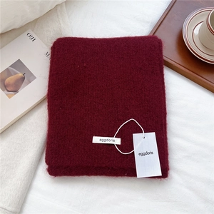 Detailed close-up of soft burgundy wool blend scarf with premium knitted texture and tag