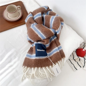 Detail of wool blend striped scarf with thick tassels and brand label on soft surface