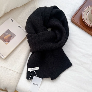 Detail shot of a black wool knit scarf showing its soft texture and white brand label
