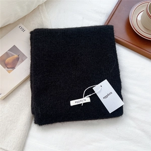 Close-up of black fluffy wool knit scarf texture with brand tag in a cozy winter setting