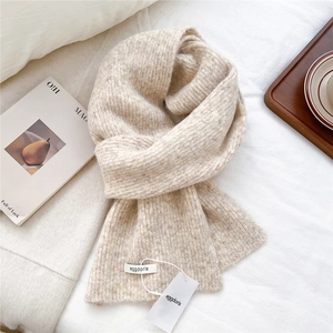 Close-up of thick knit texture and brand label on cream wool scarf on white bedding
