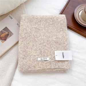 Detail of soft knit wool scarf with ribbed texture and brand tag on white bedding