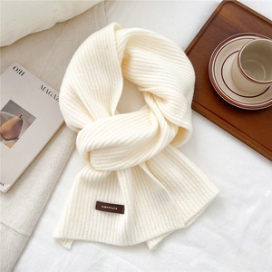 Detailed close-up of ribbed knit scarf texture with a woven label on a cozy bed scene