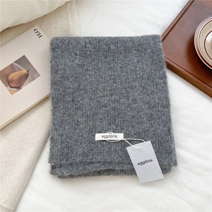 Close-up of gray wool knit scarf texture with brand label on soft white linen background