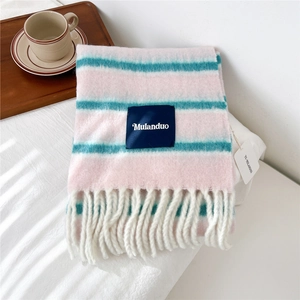 Close-up of pink and blue striped knit wool scarf with long white tassels on a bed