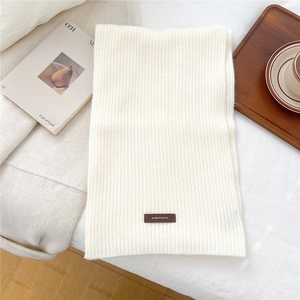 Close-up of white ribbed knit scarf featuring a vintage leather label on a cozy tray