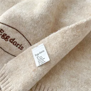 Detail of oatmeal knit scarf featuring Egg Doris embroidery and fabric composition label