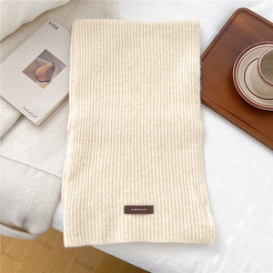Detailed view of the ribbed knit texture and brown brand tag on the cream winter scarf