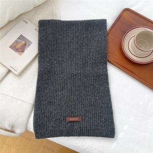 Close-up of thick grey ribbed knit scarf with a premium brown leather logo tag