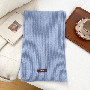 Close-up of light blue chunky knit scarf texture with a brown leather logo tag detail