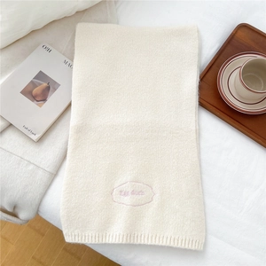 Detail of soft cream knitted scarf featuring elegant pink embroidered Egg doris logo