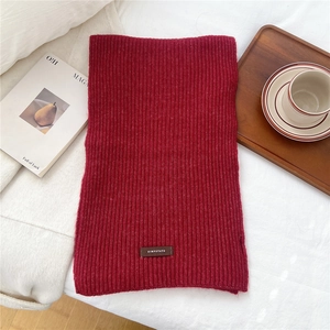 Close-up of red ribbed knit scarf with a leather brand tag on a cozy home background