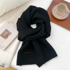 Close-up of thick black knitted scarf with an orange embroidered Egg Doris label tag