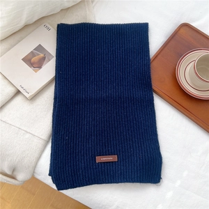 Detail of navy blue ribbed knit scarf with a brown decorative tag on a white fabric surface
