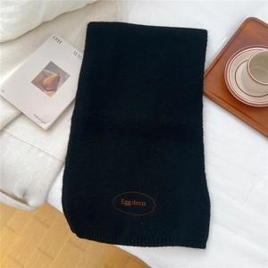 Close-up of black knitted scarf featuring orange embroidered logo on white bedding