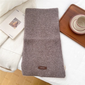 Detail of soft ribbed knit scarf in brownish purple with a leather brand tag on white bedding