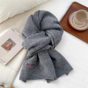 Close-up of dark grey knitted scarf with red Egg Days embroidery on soft white bedding