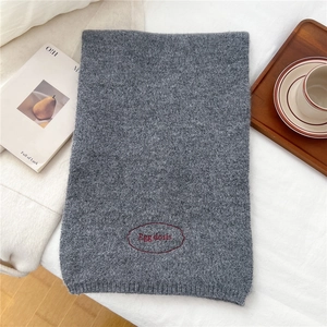Detail of grey knitted scarf showing ribbed texture and red embroidered Egg doris logo