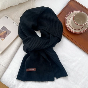 Close-up of black ribbed knit scarf featuring a leather brand tag in a cozy home setting