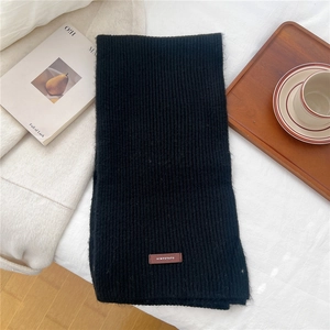 Close-up of black ribbed knit scarf with a premium brown leather brand patch