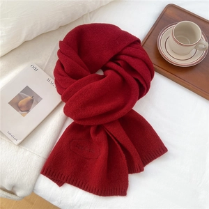 Detail of red knitted scarf featuring a textured wool weave and elegant embroidered logo